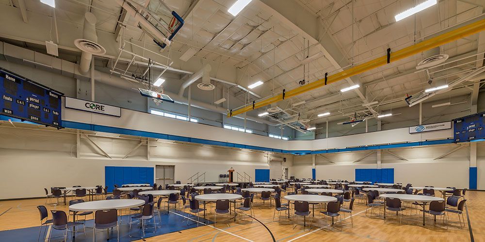 A large gym with tables and chairs and a basketball hoop.