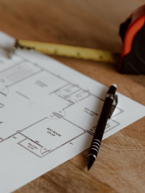 A pen is sitting on top of a floor plan next to a tape measure.