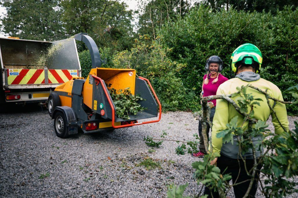 Two arborists standing behind a woodchipper.