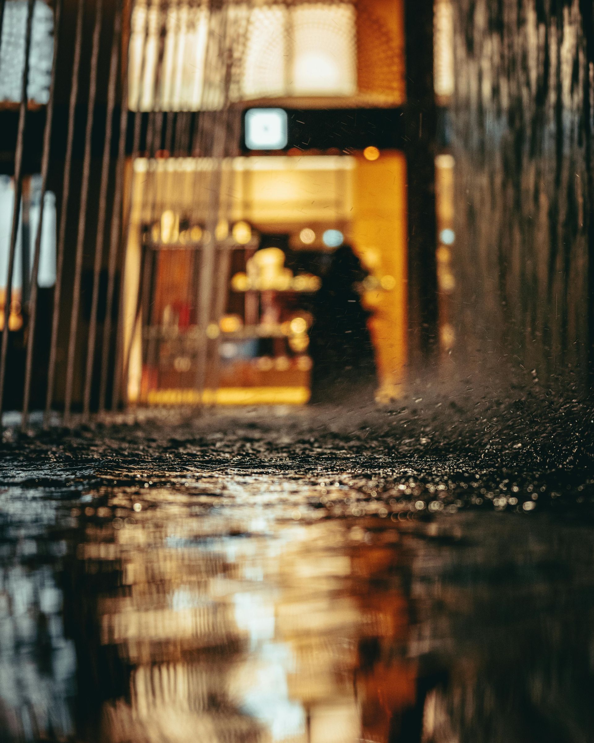 Blurred view of a lit storefront through a rainy window, with water droplets visible on the glass
