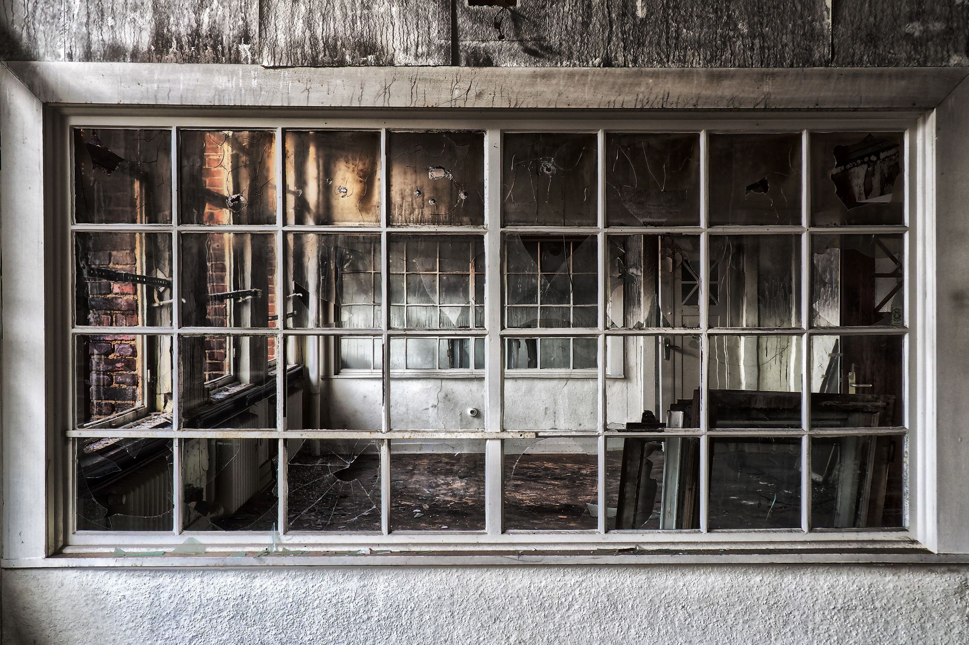 A grid-paned window looking into a derelict, soot-covered room with exposed brick, after fire.