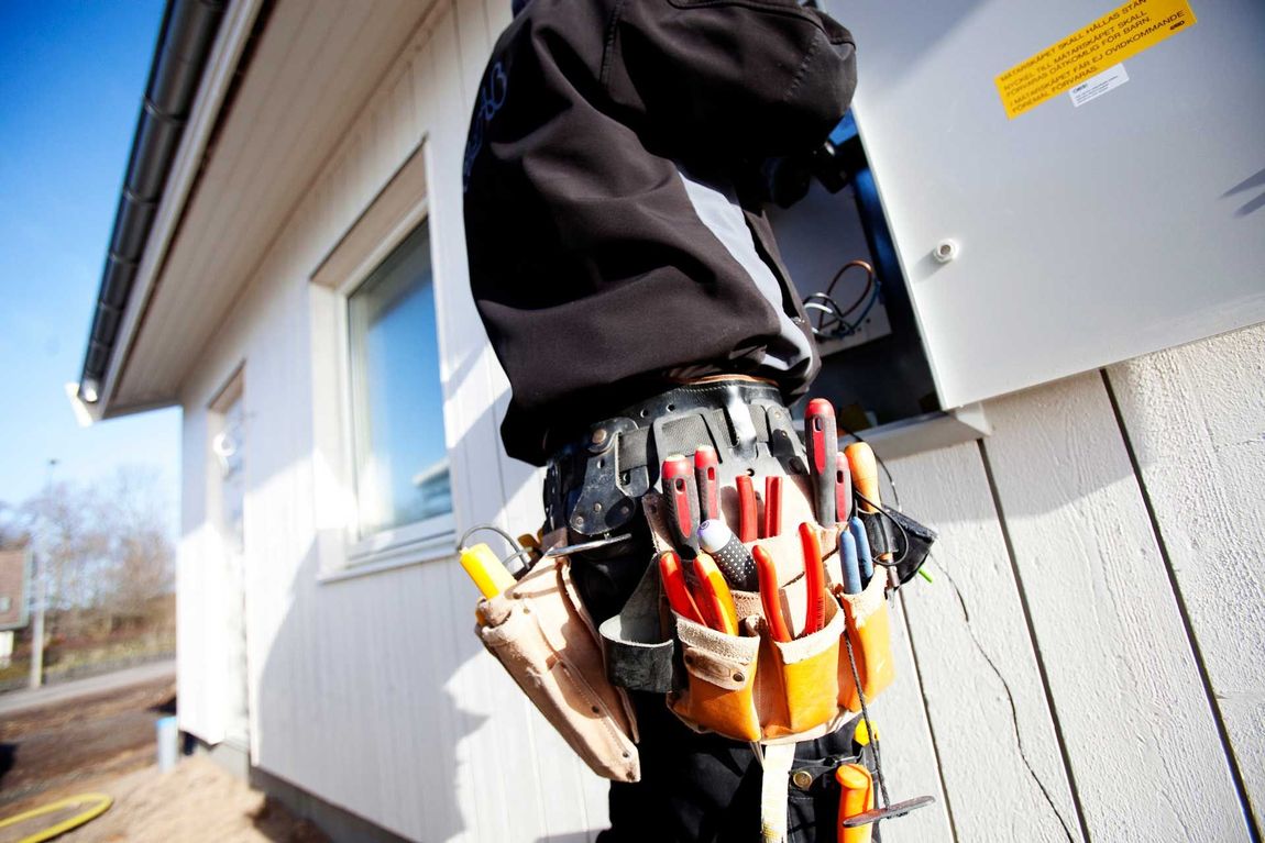 A man wearing a tool belt is standing in front of a building