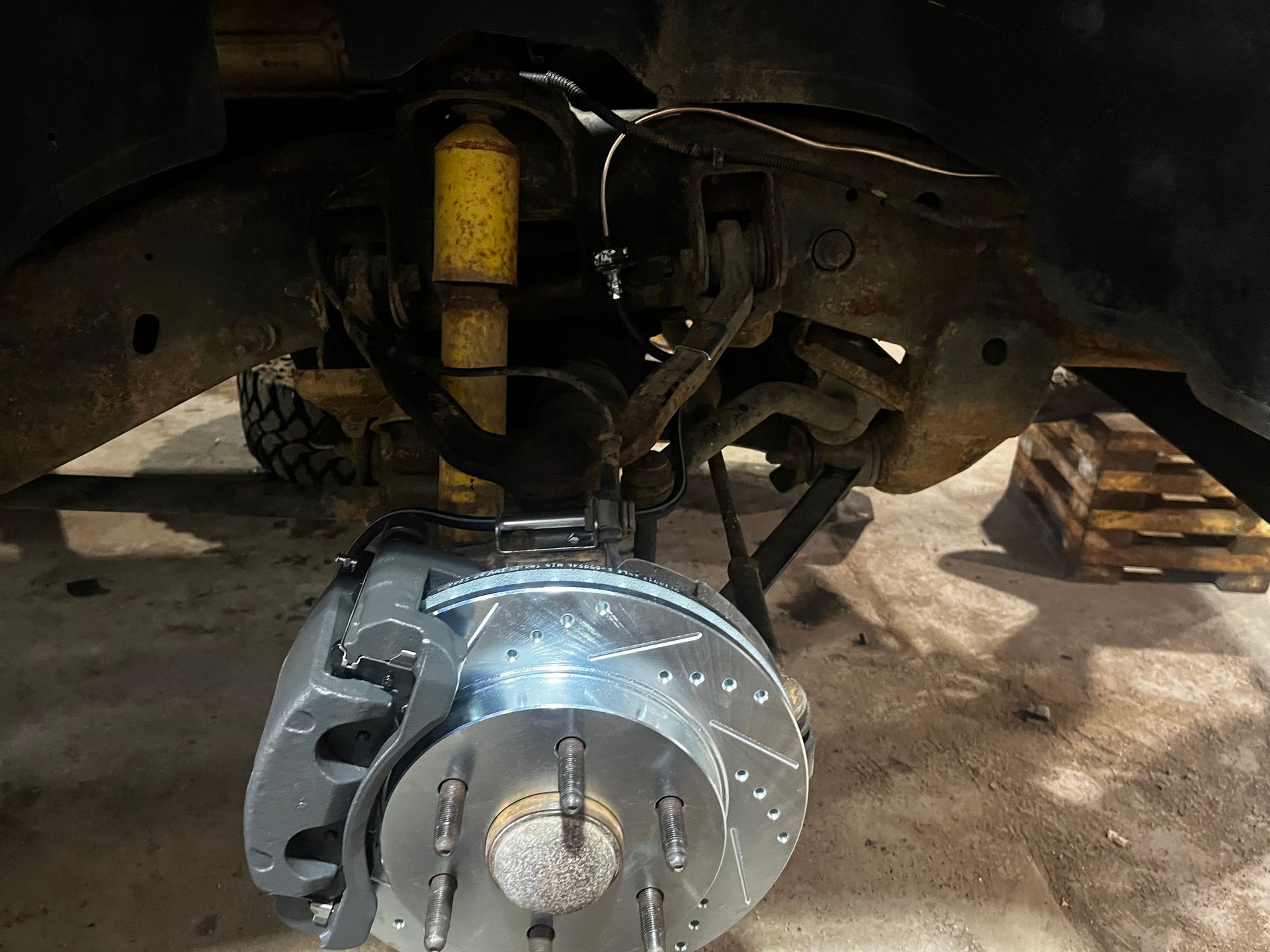 Truck's front wheel suspension with new gray brake rotor and caliper. Yellow shock absorber visible.