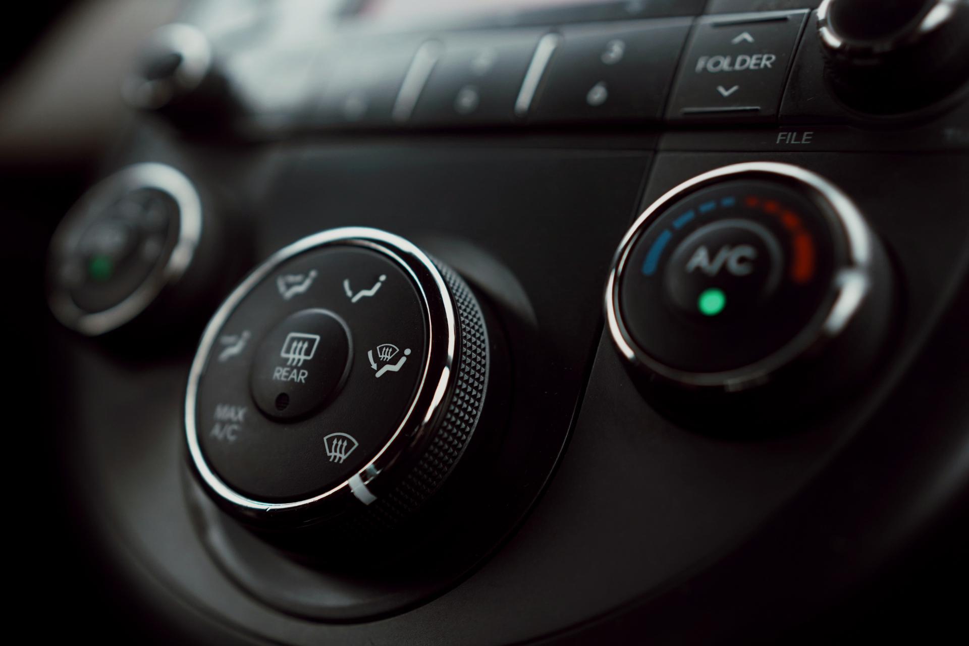 Car dashboard controls: climate knobs, including A/C and defroster settings; black with silver accents.