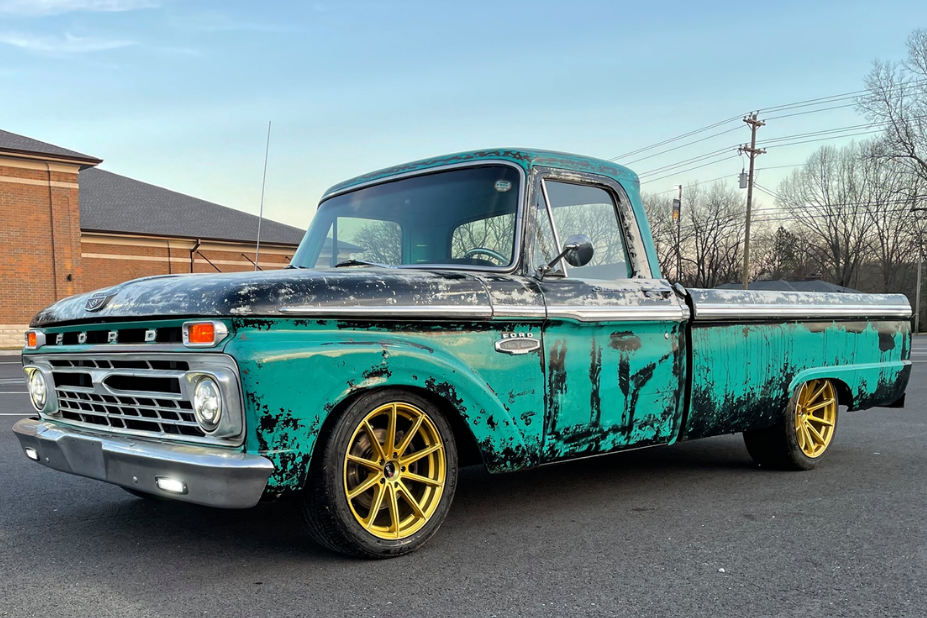 Vintage turquoise Ford pickup truck with gold wheels, worn paint, parked on asphalt.