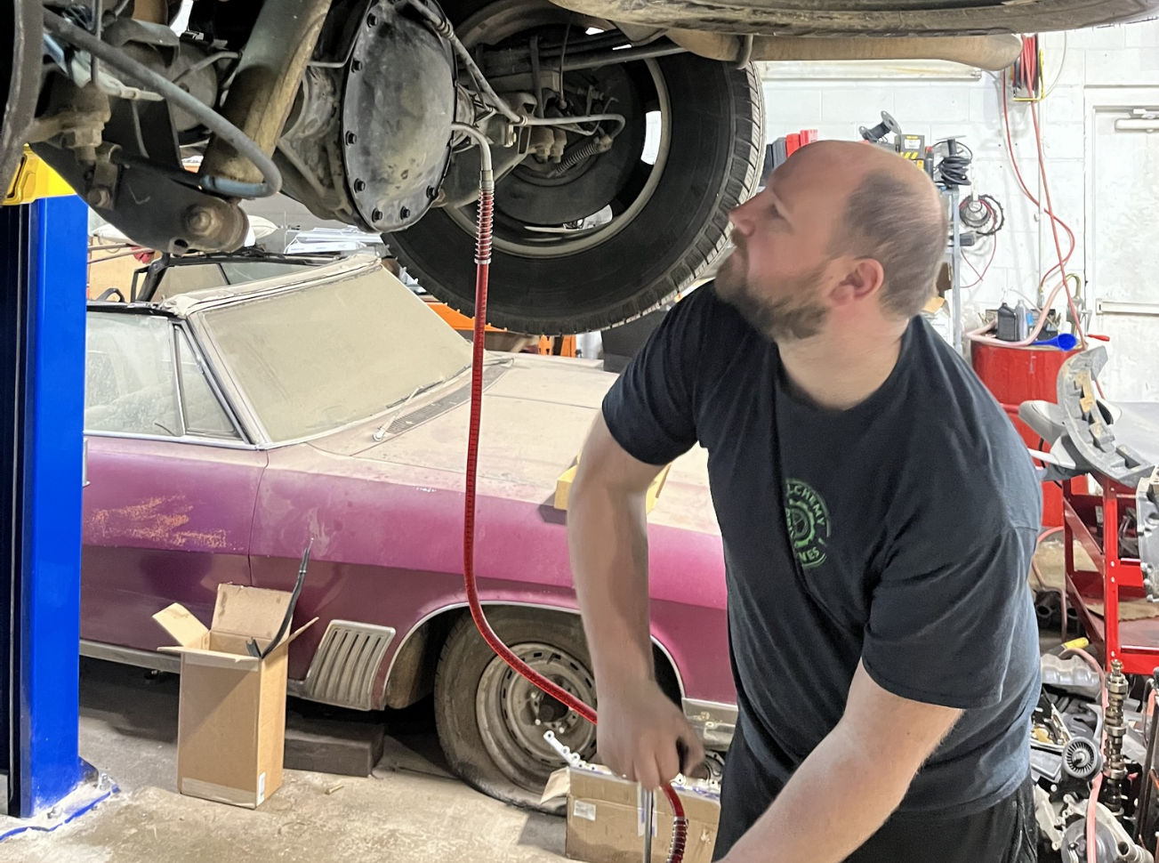 Mechanic under a car, draining fluid. Pink car, shop setting.