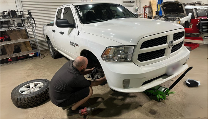 Man changing a tire on a white Ram pickup truck inside a garage.