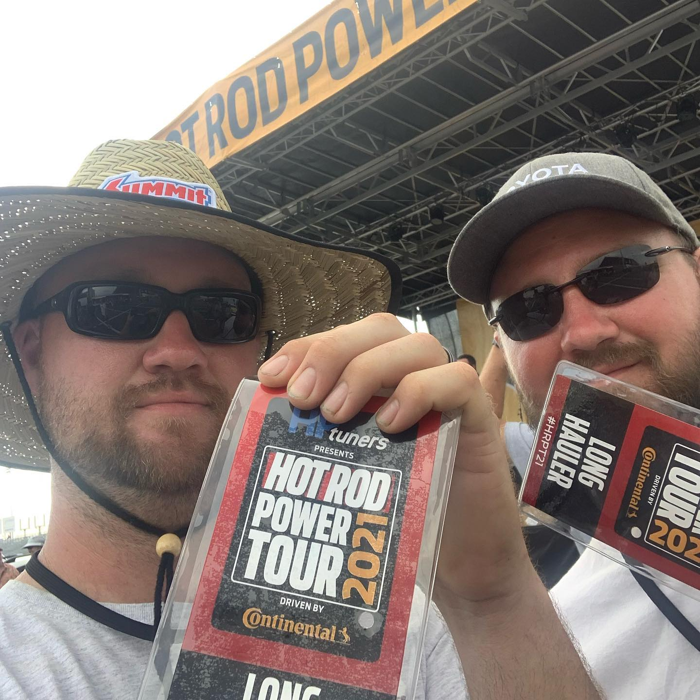 Two men at Hot Rod Power Tour 2021. One holds a pass, both wear sunglasses and hats.