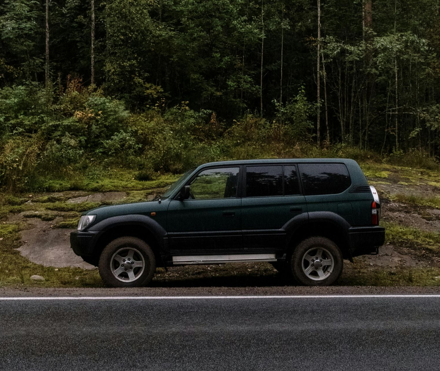 Green SUV parked on the side of a road in a wooded area.