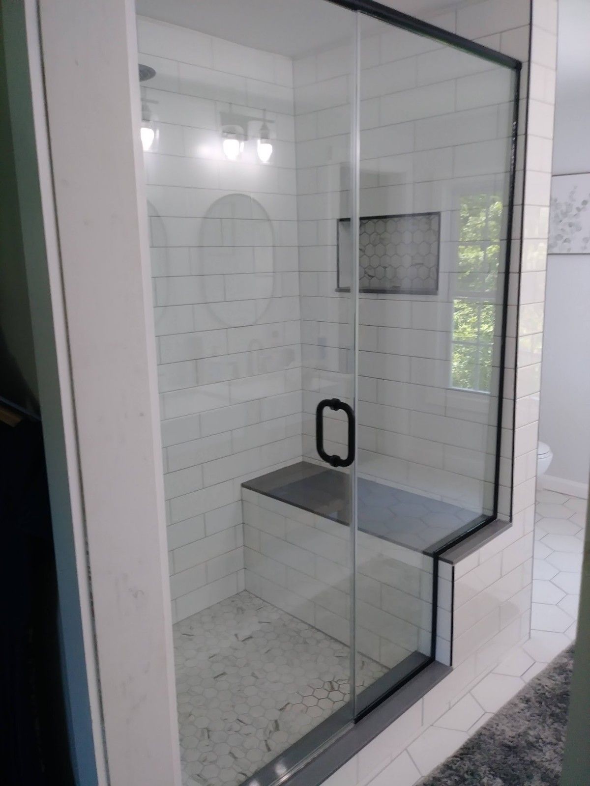 A bathroom with a walk in shower with a glass door and a bench.