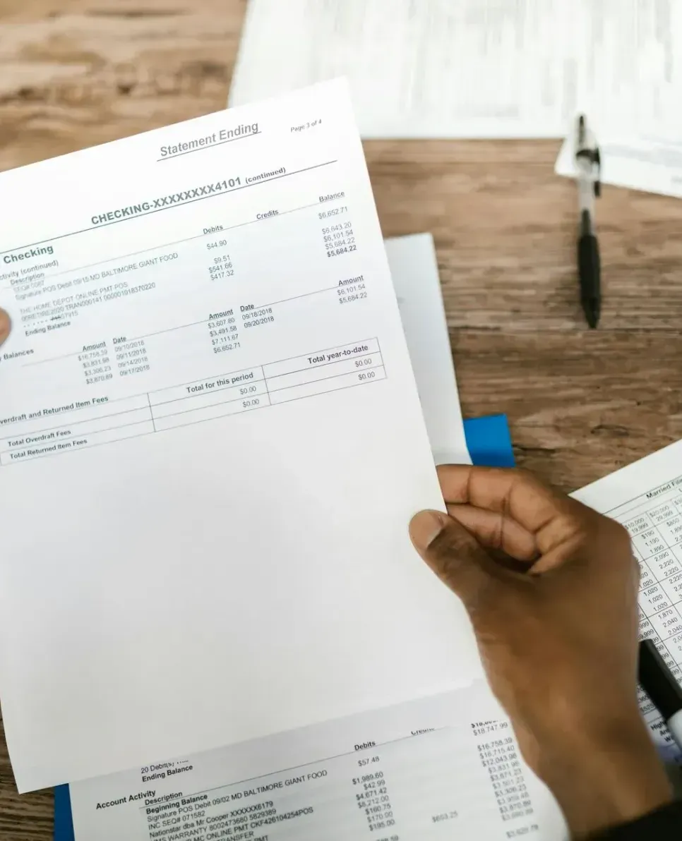 A person is holding a piece of paper in front of a wooden table.