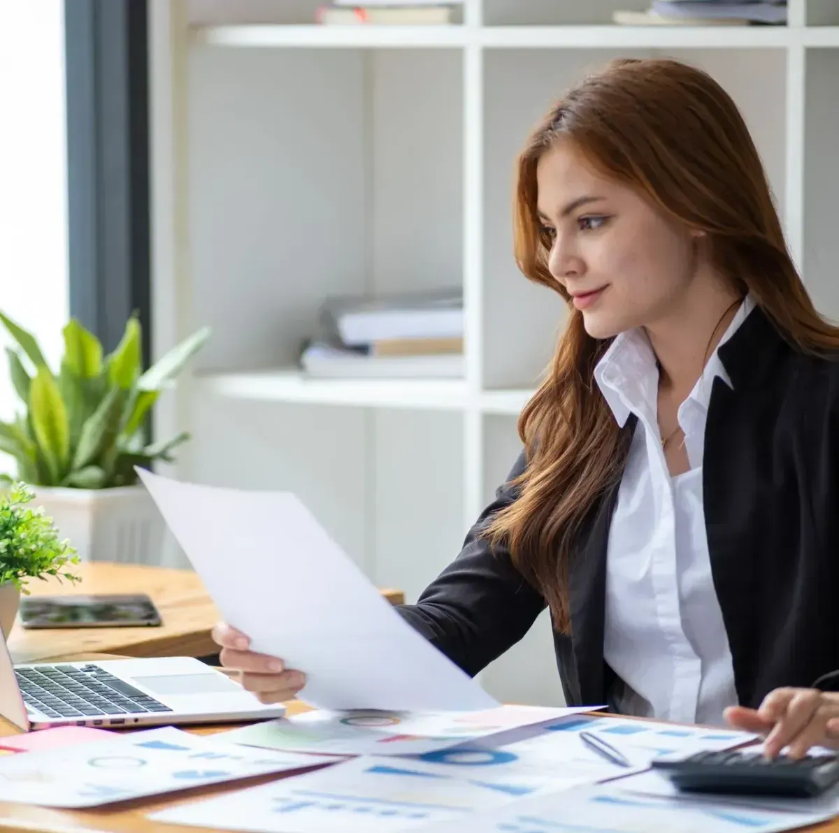 A woman is sitting at a desk with a laptop and a calculator.