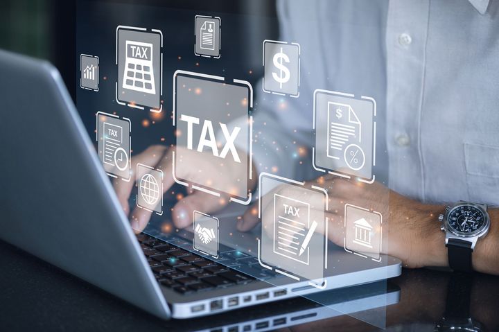 A man is using a laptop computer with a tax icon on the screen.