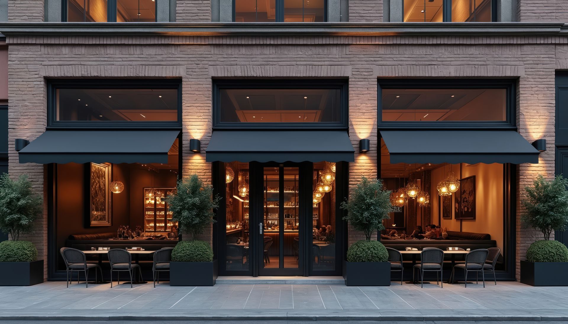 Brick storefront café with black awnings, warm lights, and outdoor seating at dusk