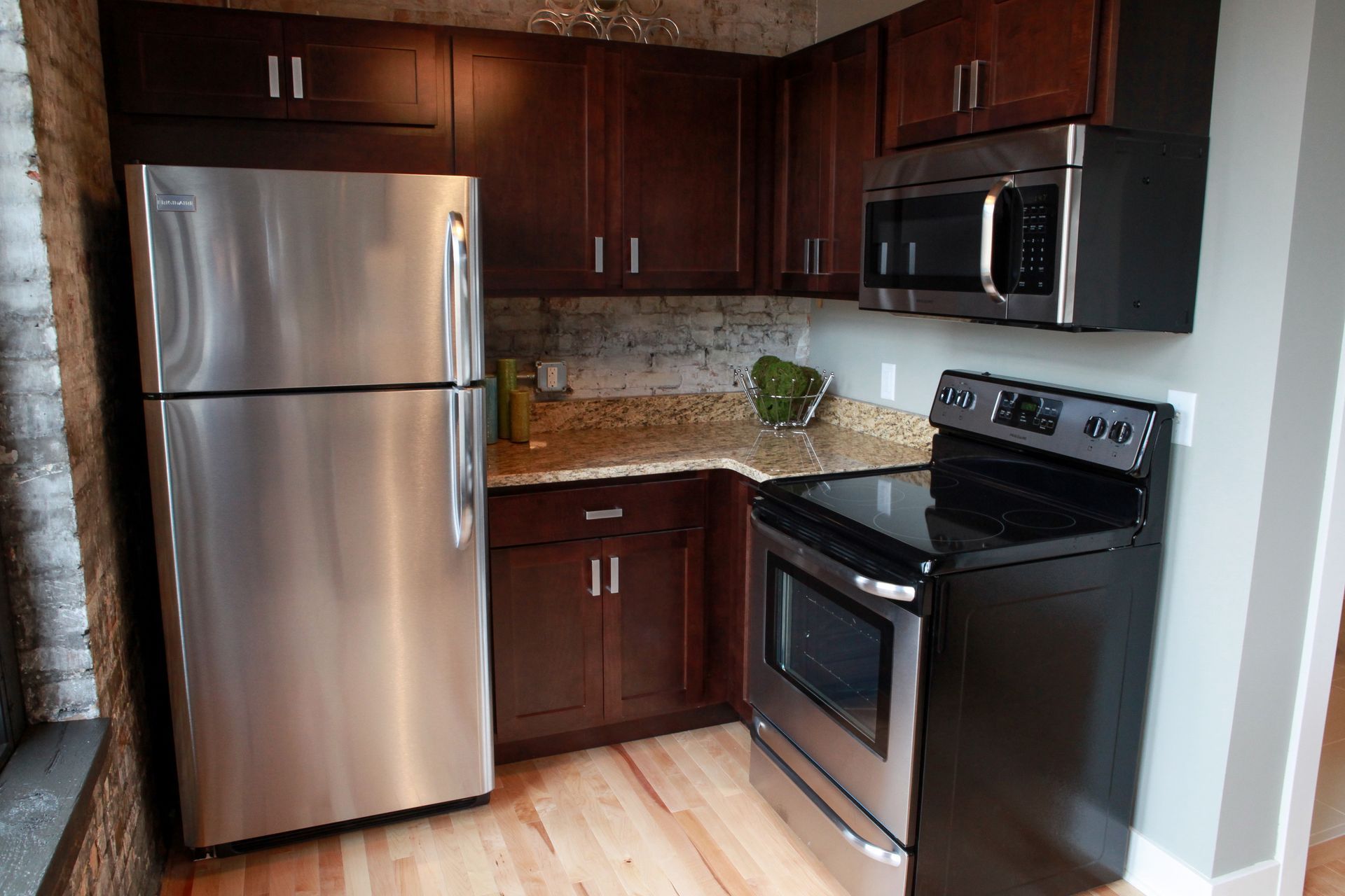 Compact kitchen with stainless steel fridge, dark cabinets, granite countertop, and black stove and microwave.