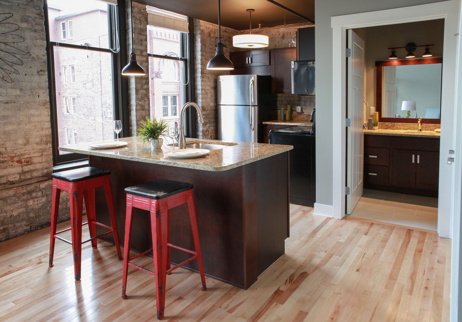 Modern kitchen with dark island, red stools, hardwood floors, and adjacent bathroom visible through a doorway