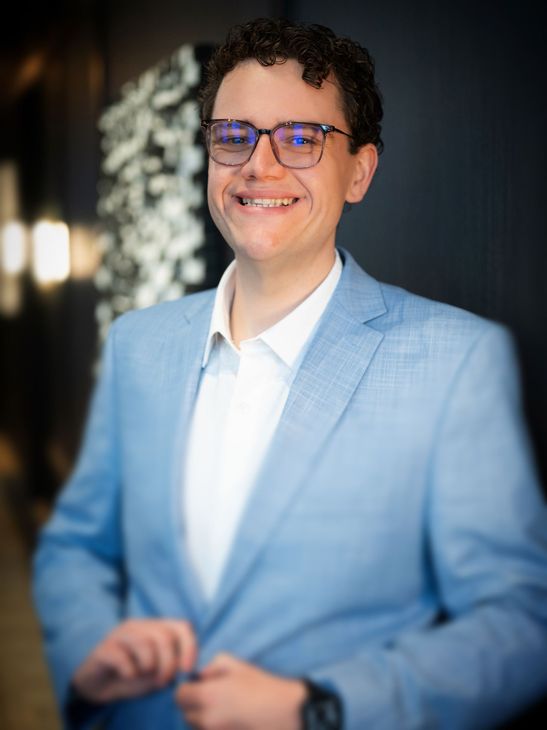 a smiling man with glasses buttoning his suit jacket
