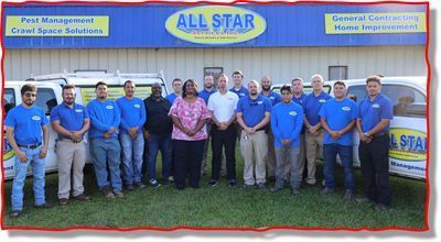 A group of employees in blue company shirts stand together in front of an All Star facility with service vehicles.