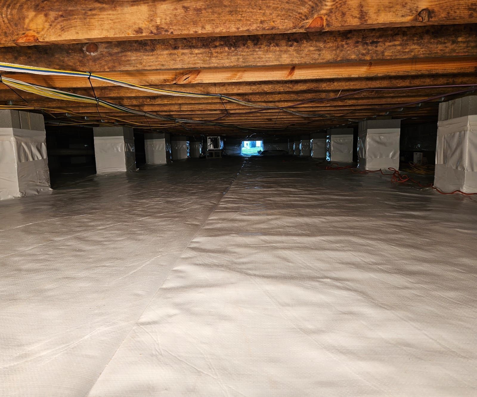 A crawl space featuring a clean white vapor barrier covering the ground and white-wrapped structural support piers.