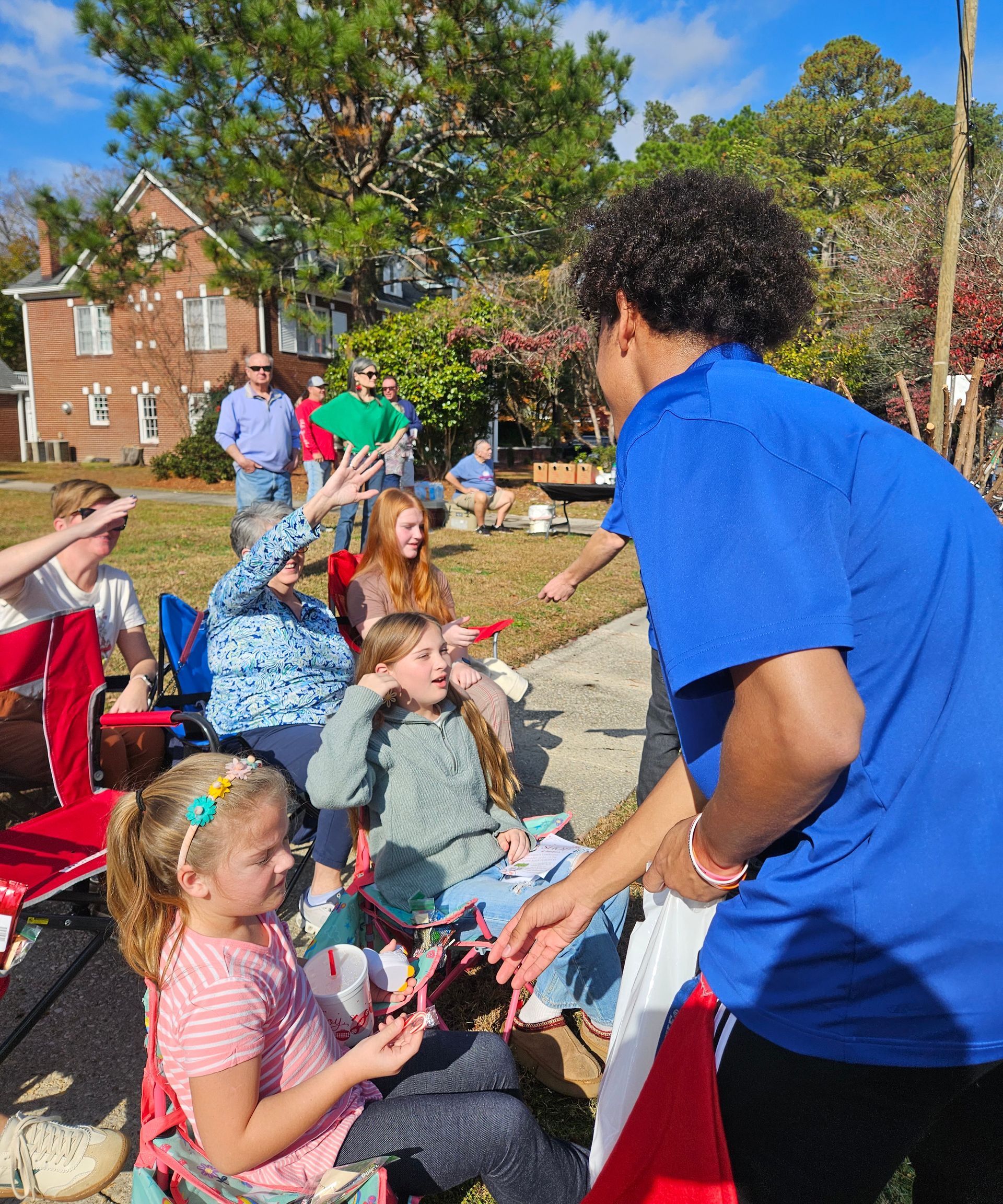 A person in a blue shirt interacts with seated individuals holding small model airplanes outdoors on a sunny day.