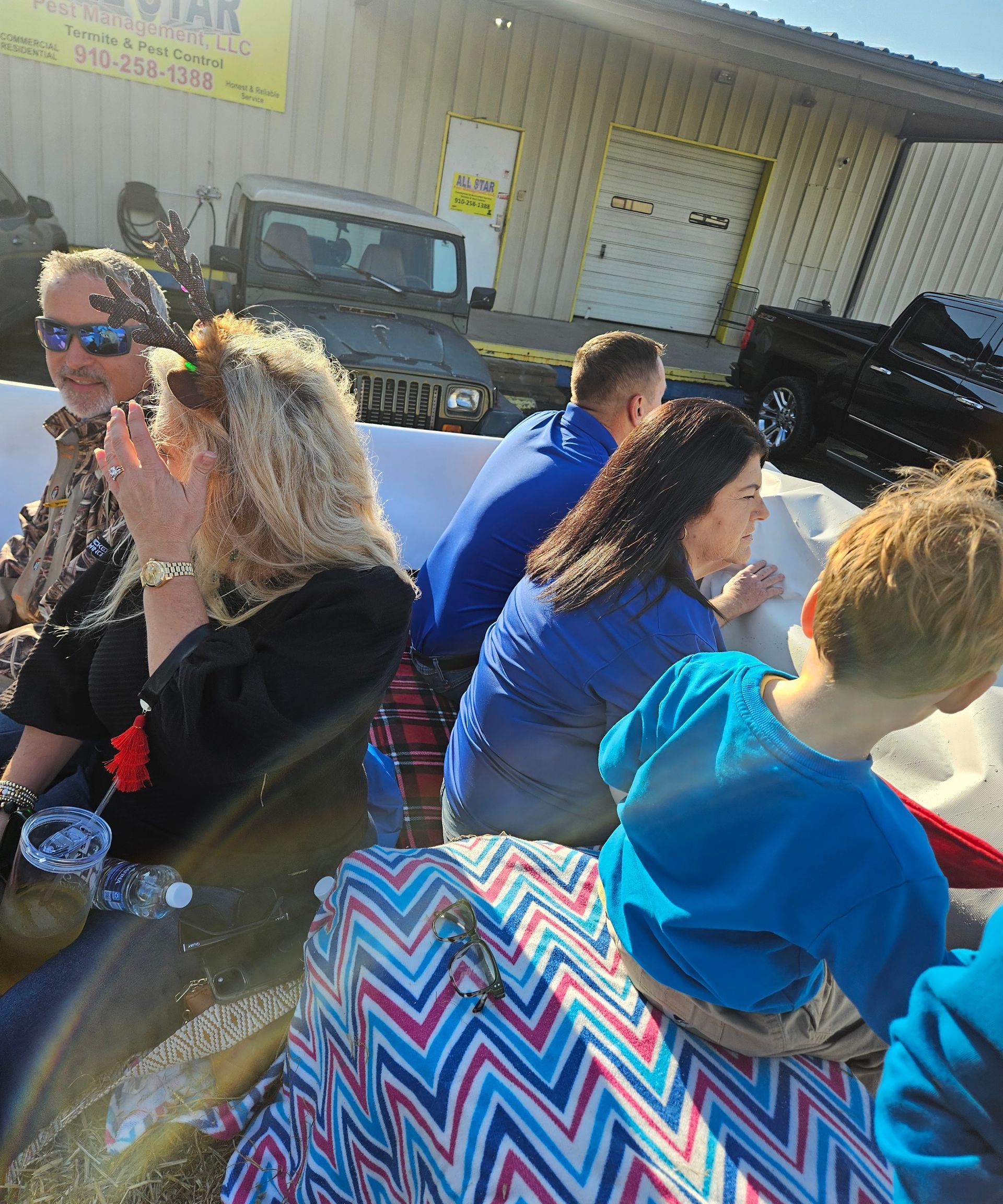 People sit on a flatbed trailer decorated with a colorful chevron-patterned cloth, parked in front of a building.