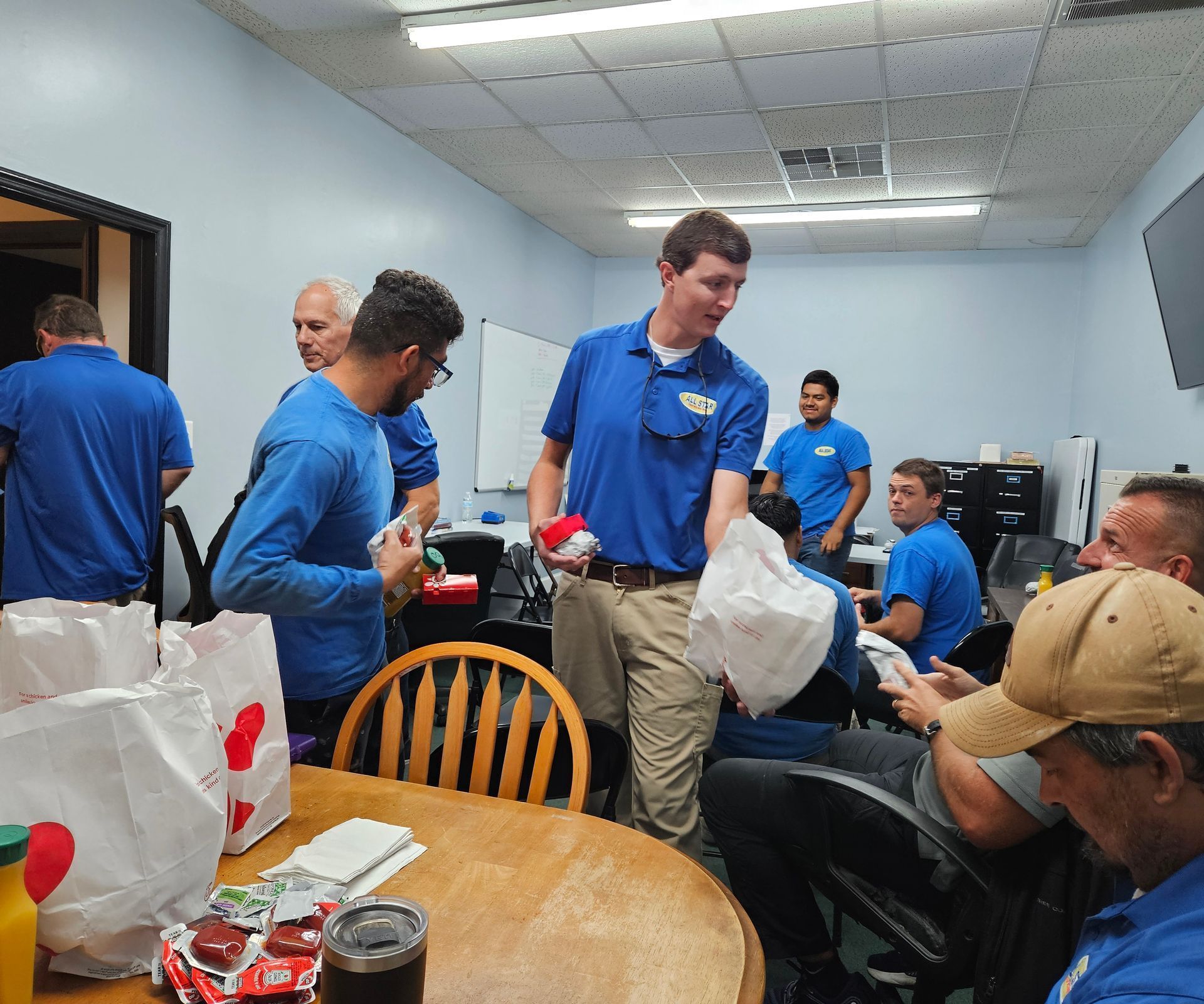 A group of people wearing matching blue shirts distribute bagged meals in an office meeting room.