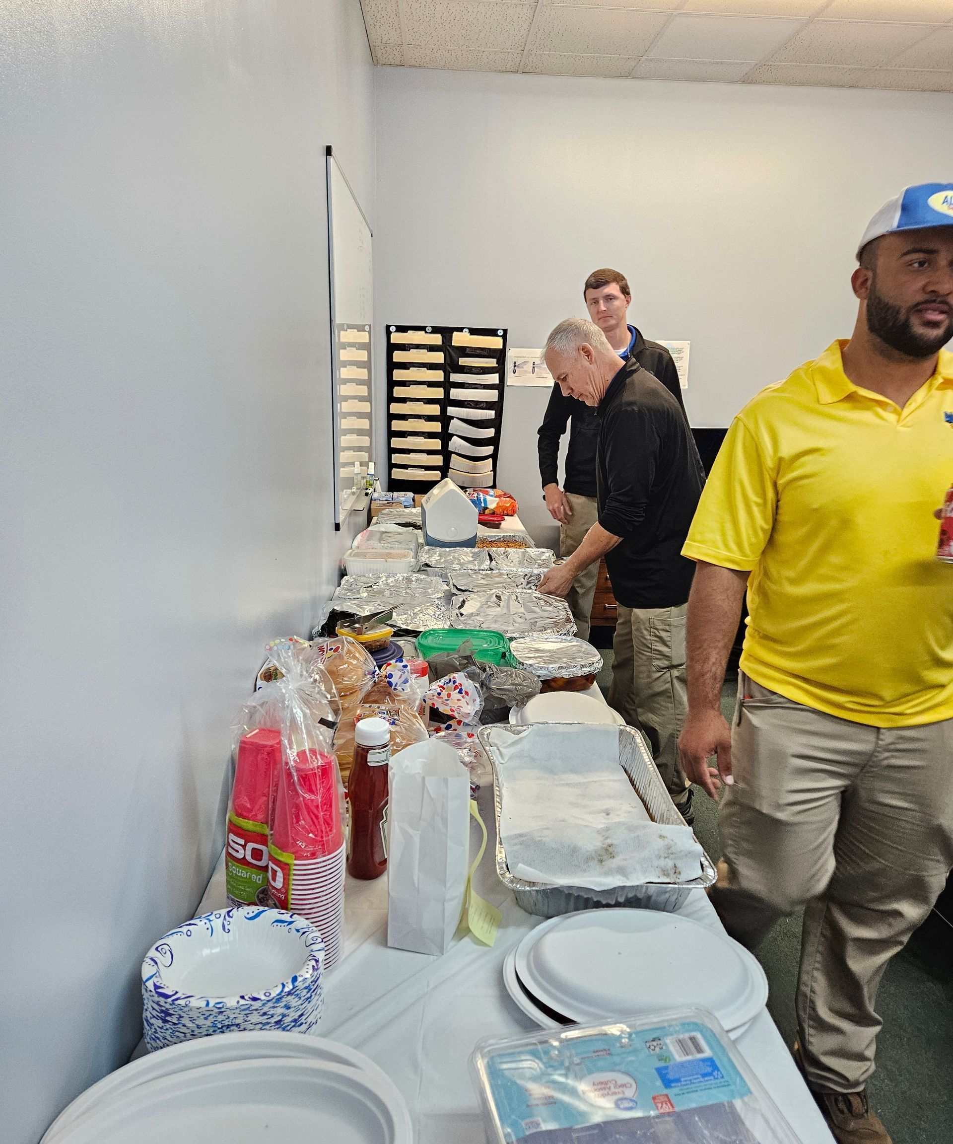 A group of people standing near a buffet table with plates, snacks, and condiments in an indoor setting.