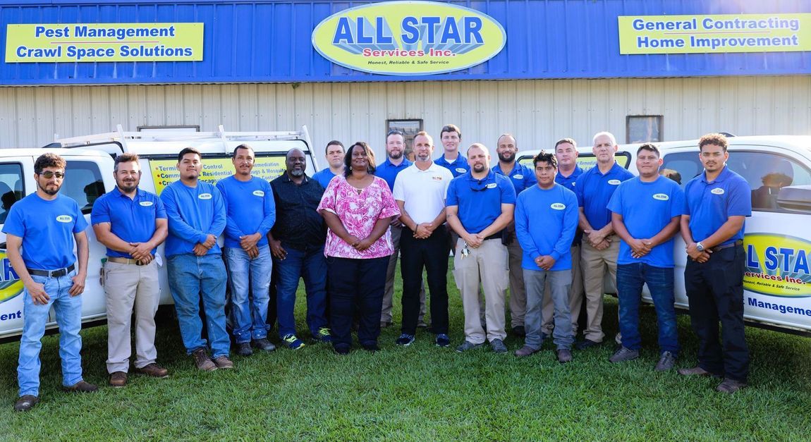 A group of people wearing blue uniforms and casual clothes posing in front of All Star service vans and their building.