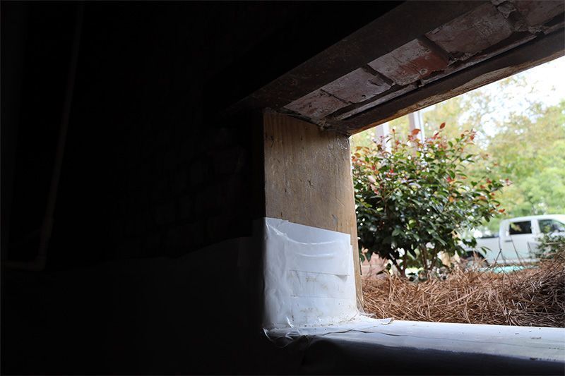 A view through a basement window showing a plywood frame, white sealant, and a white pickup truck parked outside.