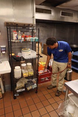 A person wearing a blue polo shirt and khaki pants uses a chemical sprayer to treat a metal wire rack.