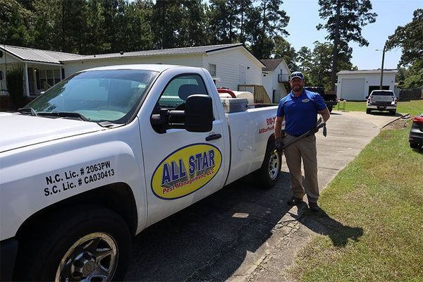 A worker in a blue uniform stands next to a white All Star professional services truck in a residential driveway.