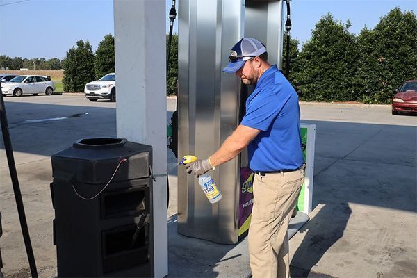 A person in a blue shirt sanitizing a trash can at a gas station.