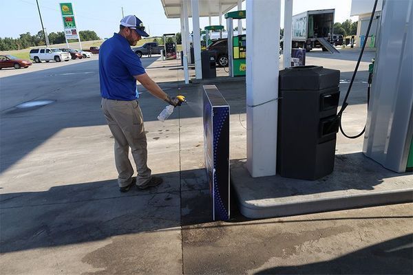 A person wearing a blue shirt and khaki pants sprays a cleaner onto a display sign at a gas station.
