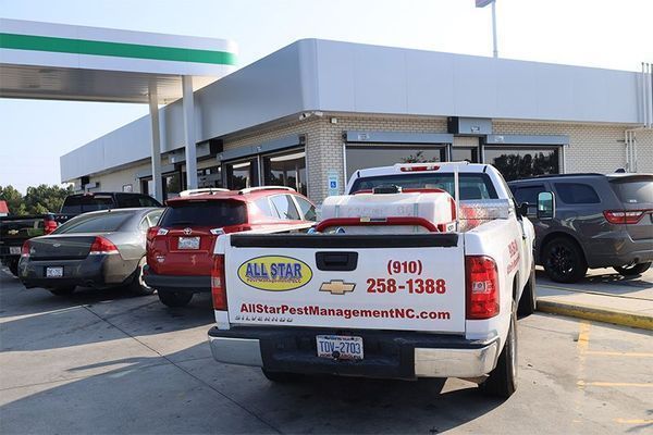 A white All Star Pest Management pickup truck parked at a gas station with other cars nearby.