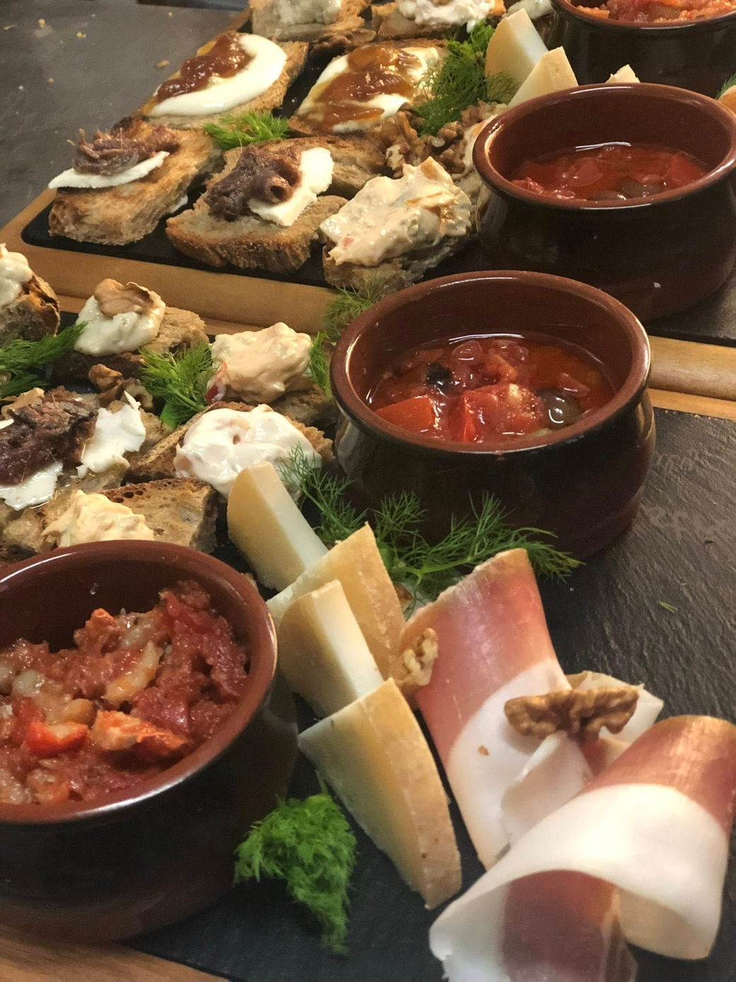 Tagliere di salumi con vari formaggi, carni, pane e salsa rossa in piccole ciotole marroni.