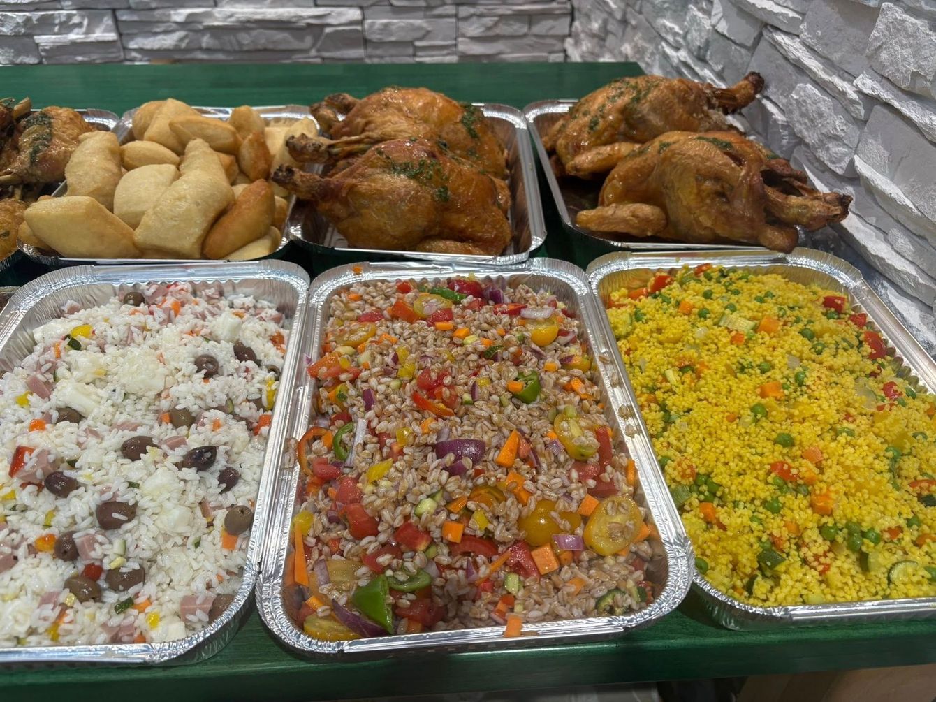 Vassoi con pollo cotto, piatti di riso e pasticcini, disposti su una superficie verde.