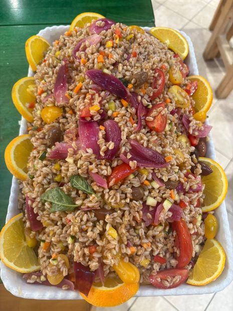 Insalata d'orzo con pomodori, cipolla rossa, carote e fette d'arancia in un vassoio rettangolare bianco.