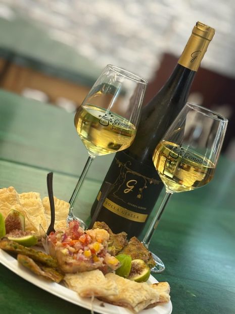 Bottiglia di vino e bicchieri con stuzzichini su un piatto, superficie verde.