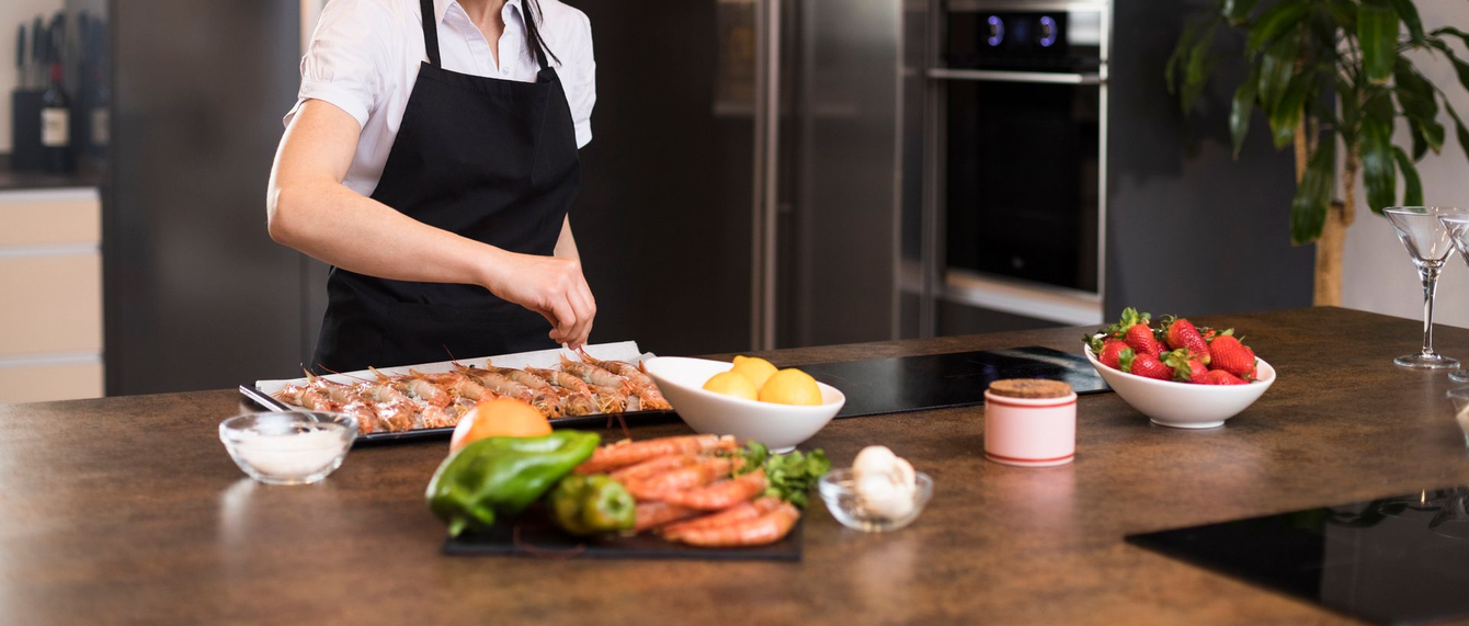 Una persona in cucina prepara il cibo su un piano di lavoro con ingredienti come fragole, gamberetti e verdure.