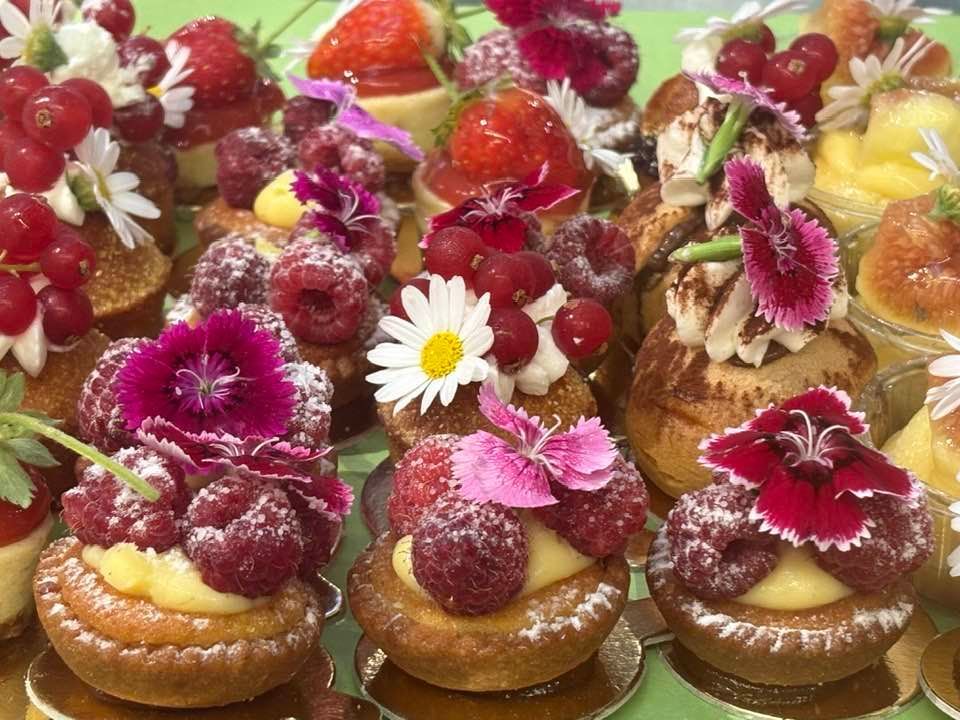 Primo piano di mini crostatine di frutta assortite, guarnite con bacche e fiori commestibili; spolverate con zucchero a velo.