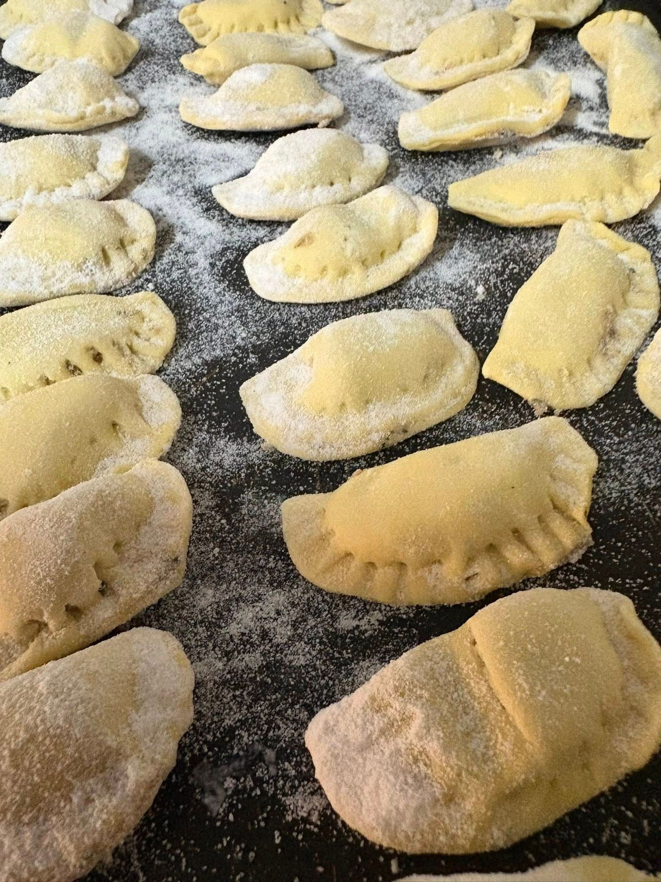 Gnocchi crudi e ripieni, spolverati di farina e disposti su una superficie scura.