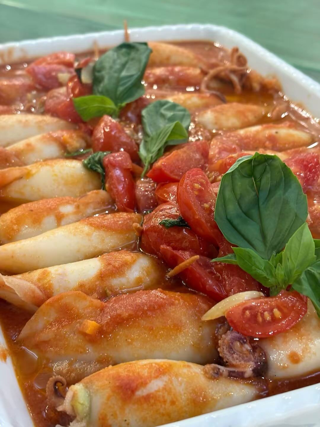 Calamari stufati in salsa di pomodoro, guarnito con basilico fresco.