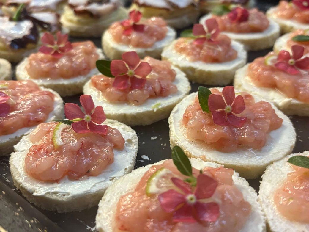 Primo piano di bocconcini di antipasto con guarnizione rosa, piccoli fiori e limone.