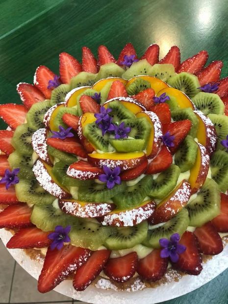 Crostata di frutta con fragole, kiwi, pesca e fiori viola.
