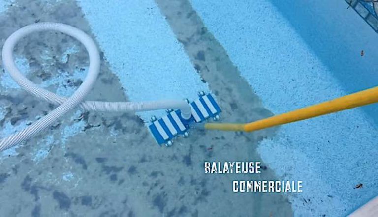 Une tête d'aspirateur de piscine bleue fixée à une perche jaune et un tuyau blanc nettoie les saletés du fond d'une piscine.