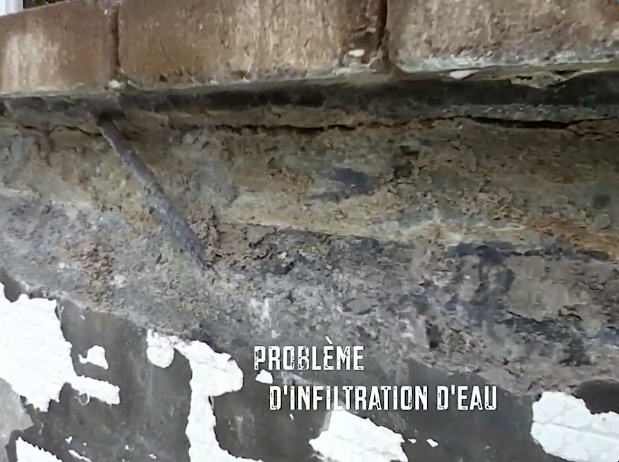Un mur de maçonnerie endommagé présentant des infiltrations d'eau, avec un plâtre qui s'écaille et un mortier apparent et friable sous la maçonnerie.
