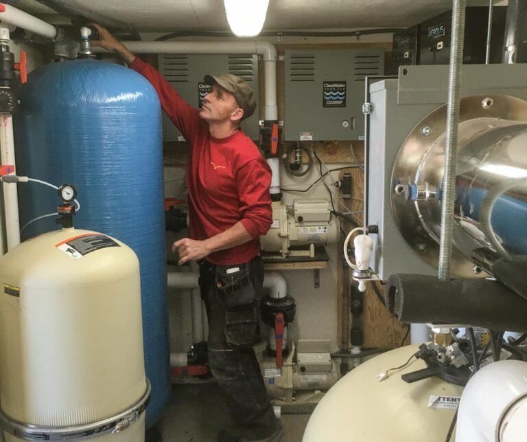Un technicien en chemise rouge travaille sur les systèmes de plomberie et de filtration d'eau dans une salle des équipements.