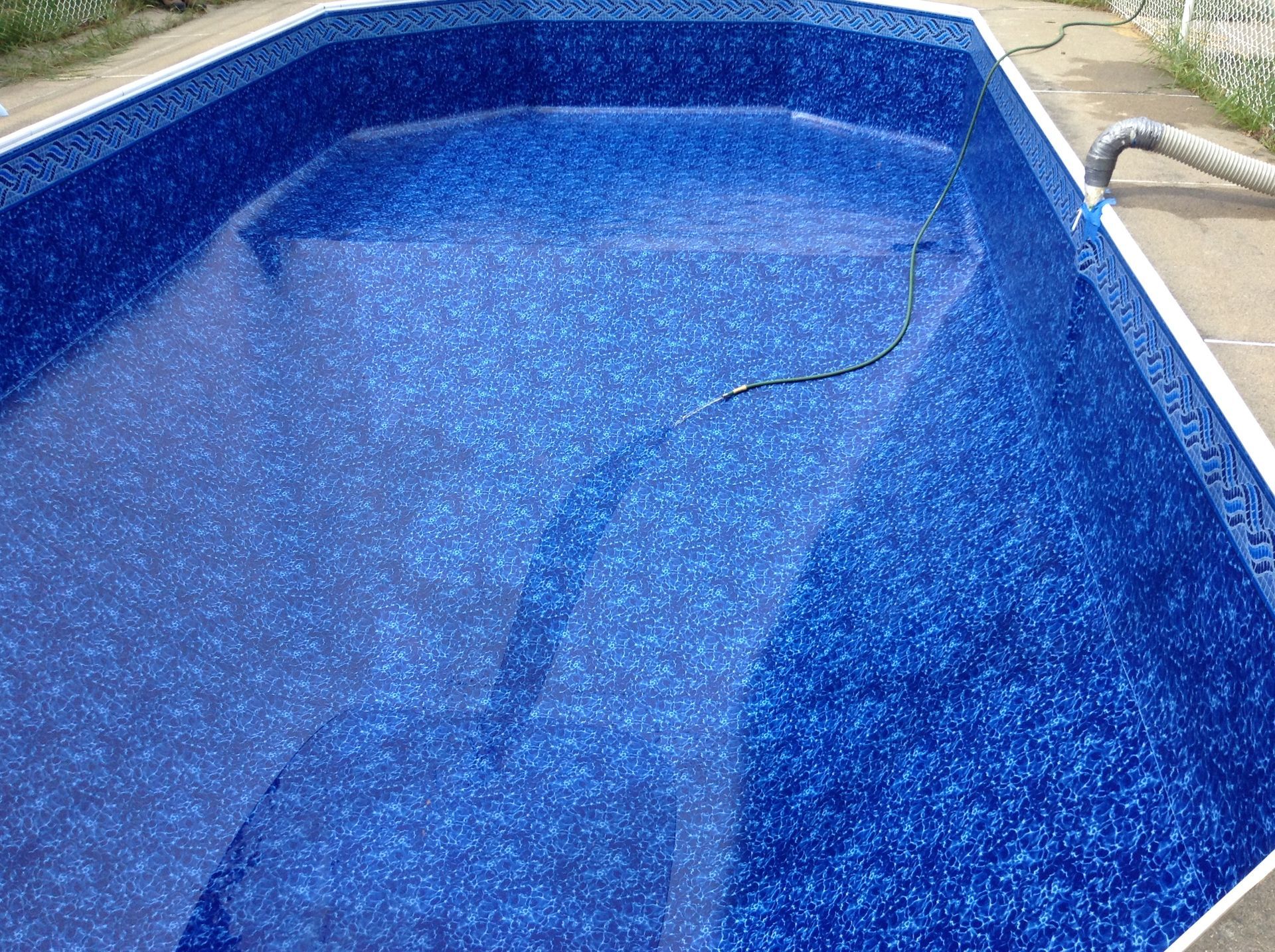 Une piscine rectangulaire, revêtue de vinyle bleu foncé, avec un tuyau de nettoyage à l'intérieur.