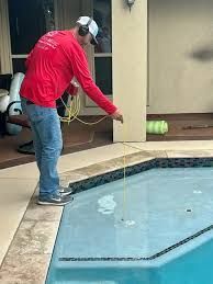 Une personne vêtue d'une chemise rouge et d'un jean utilise un outil relié à un cordon jaune pour inspecter l'eau d'une piscine résidentielle.