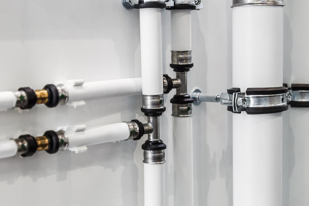 White Pipes With Silver Clamps and Joints Against a White Wall — HFB Plumbing & Gas in Redlynch, QLD